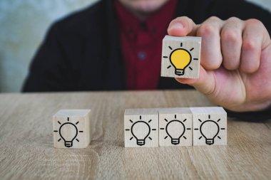 bir el, diğer tüm lambalar söndürüldüğünde yanan lambalı bir küp tutar, bu da Yeni Fikir'i, yenilik ve çözüm kavramlarını sembolize eder.