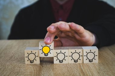 bir el, diğer tüm lambalar söndürüldüğünde yanan lambalı bir küp tutar, bu da Yeni Fikir'i, yenilik ve çözüm kavramlarını sembolize eder.