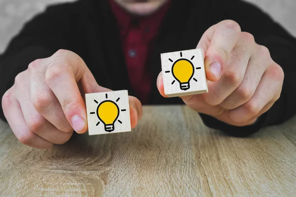 Una persona tiene en sus manos dos cubos de madera con imágenes de lámparas en llamas, lo que simboliza la elección de una nueva idea, el concepto de innovación y soluciones . —  Fotos de Stock