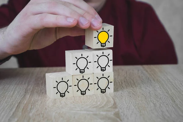 Een hand houdt een kubus met een brandende lamp wanneer alle andere lampen zijn gedoofd, wat het nieuwe idee symboliseert, de concepten van innovatie en oplossingen. — Stockfoto