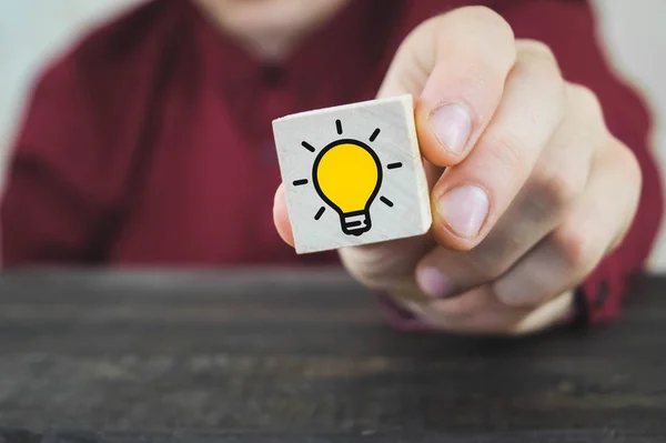 手选择的木立方体，木桌上有黄色灯泡符号。创新理念、创新理念和解决方案. — 图库照片