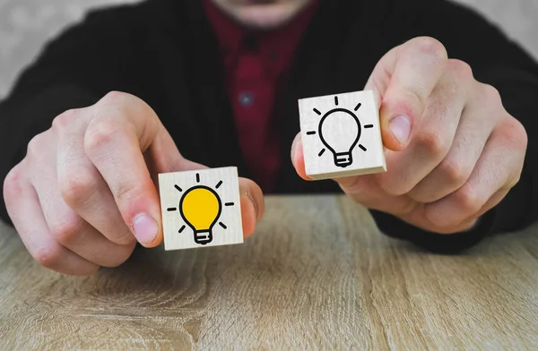 Twee houten blokjes in de handen van een persoon in een pak, waarvan er een is verlicht in geel, die het nieuwe idee symboliseert, het concept van innovatie en oplossingen. — Stockfoto