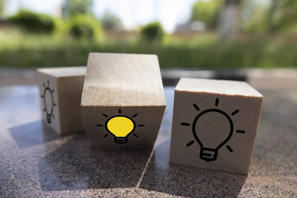 创意理念、新理念、创新理念和解决方案理念。木立方体与黄色灯泡符号在桌子上，蓝色背景，复制空间 — 图库照片
