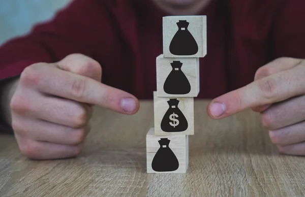 5 wooden cubes in the form of bags of money. Hand selects a bag.