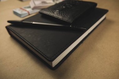 Siyah bir not defteri , ahşap arka plan üzerinde bir kalem ve dolar nakit banknotlar - finansal yönetim veya planlama kavramı, serbest yazma para kazanmak