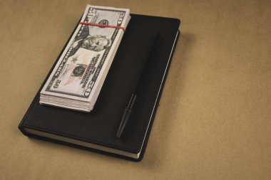 Siyah bir not defteri , ahşap arka plan üzerinde bir kalem ve dolar nakit banknotlar - finansal yönetim veya planlama kavramı, serbest yazma para kazanmak