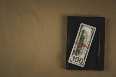 Siyah bir not defteri , ahşap arka plan üzerinde bir kalem ve dolar nakit banknotlar - finansal yönetim veya planlama kavramı, serbest yazma para kazanmak