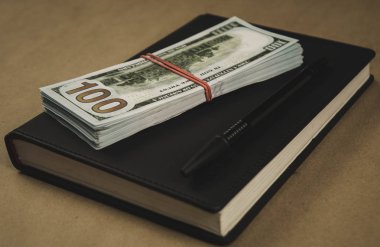 Siyah bir not defteri , ahşap arka plan üzerinde bir kalem ve dolar nakit banknotlar - finansal yönetim veya planlama kavramı, serbest yazma para kazanmak