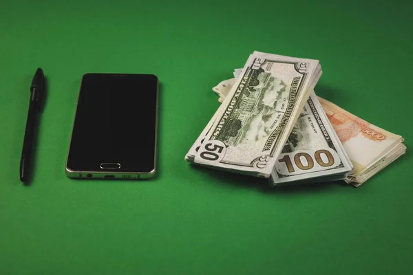 De nombreux paquets d'argent comptant, téléphone et stylo couché sur un fond vert — Photo