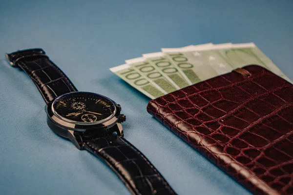 Horloge et portefeuille avec de l'argent couché sur un fond bleu — Photo