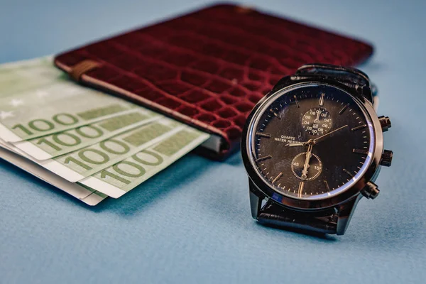 Horloge et portefeuille avec de l'argent couché sur un fond bleu — Photo