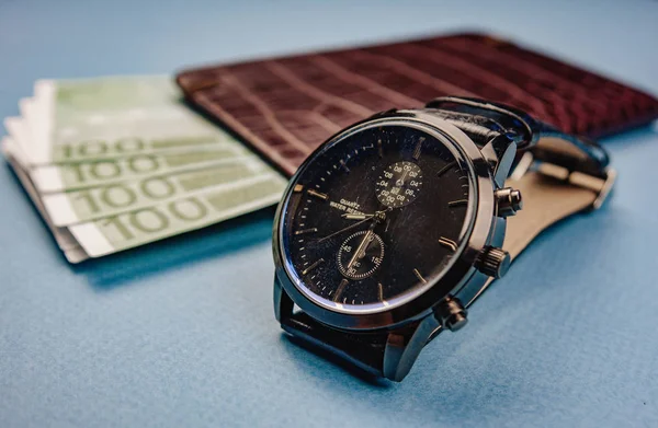 Годинник і гаманець з грошима лежать на синьому фоні — стокове фото