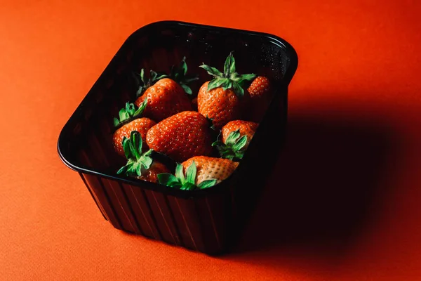 Frische saftige Erdbeeren mit Blättern in einem schwarzen Korb. Erdbeere auf rotem Hintergrund — Stockfoto