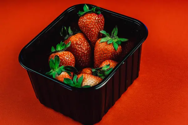 Fresh juicy strawberries with leaves in a black basket. Strawberry on a red background — Stock Photo, Image