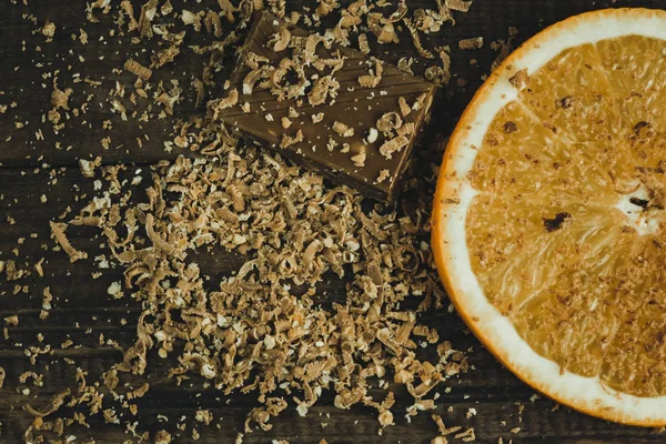 Sweet background. Cocoa powder sprinkled on surface, orange citrons and pieces of dark chocolate on black slate. Top view, copy space