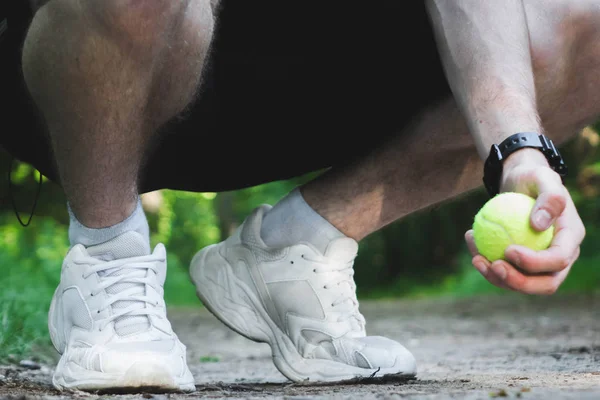 Hombre en cuclillas sostiene una pelota de tenis en su mano . — Foto de Stock