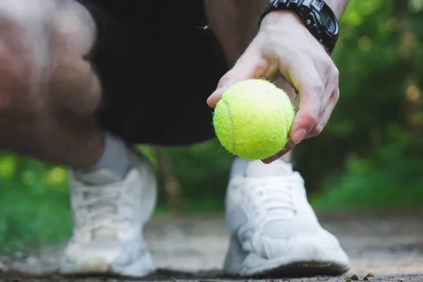 Hombre en cuclillas sostiene una pelota de tenis en su mano . — Foto de Stock