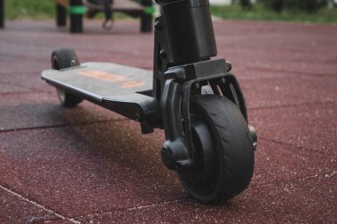siyah elektrikli scooter parkta kauçuk ped üzerinde duran, ön arka.