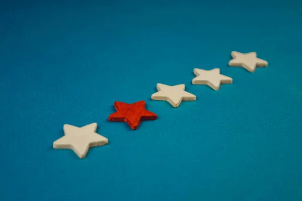 Ένα μάτσο ξύλινα αστέρια και ένα από αυτά επισημαίνεται με κόκκινο χρώμα. θέμα σε μπλε φόντο — Φωτογραφία Αρχείου