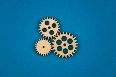 Mavi arka planda ahşap dişli. Sunumlar ve afişler için soyut arka plan. Teknoloji ve sanayi kavramı, düşünme süreci. Büyük karmaşık bir mekanizmanın parçası. Afiş.