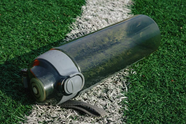 Plastic fles water liggend op gras voetbalveld. — Stockfoto