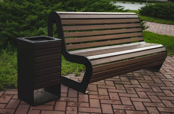 Black metal trash can near the bench on the street. — Stock Photo, Image