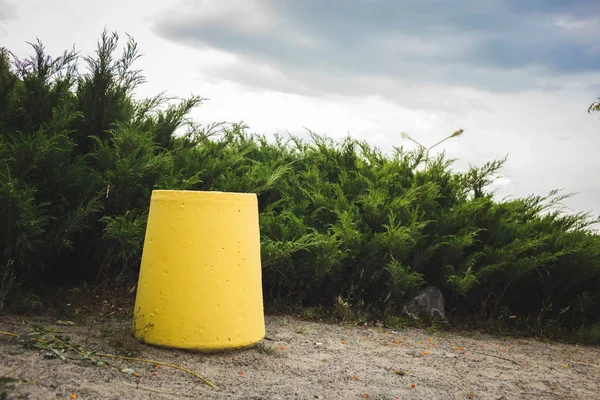 yellow trash can standing in the Park in front of thick bushes