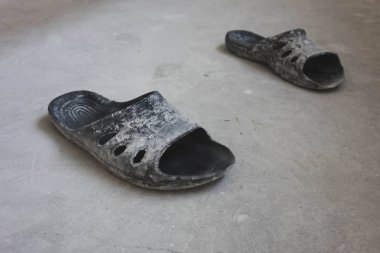 beton zemin üzerinde duran siyah kauçuk parmak arası terlik, onarım kavramı.