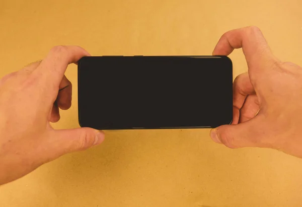 El teléfono inteligente negro se encuentra horizontalmente sobre un fondo marrón . —  Fotos de Stock
