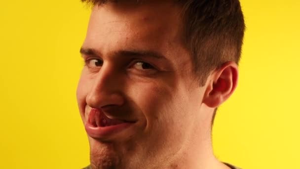 Portrait d'un jeune homme grimaçant à la caméra et izobrazhaet actions incompréhensibles sur un fond jaune — Video