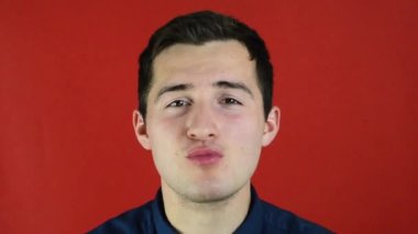 Kırmızı arka planda duran bir adam gülümseyerek elma yiyor.