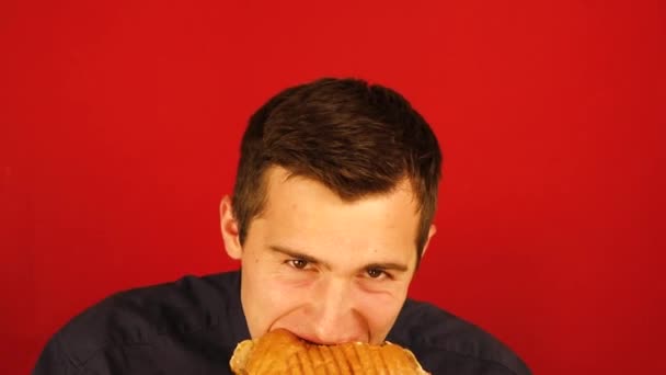 Человек усердно ест бургер на красном фоне . — стоковое видео