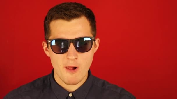 Guy in glasses hard eating popcorn from a plate on a red background — Stock Video