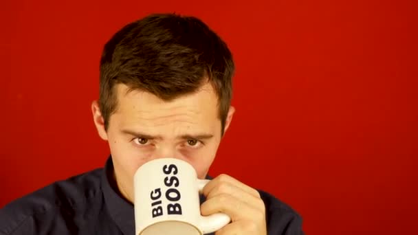 Un hombre bebe de una taza con las palabras BIG BOSS sobre un fondo rojo — Vídeos de Stock