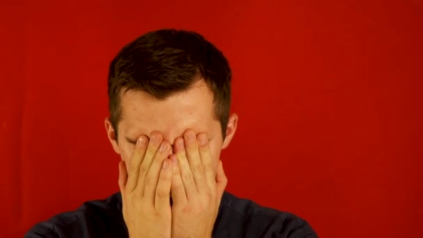 Um homem aterrorizado agarra seu rosto contra um fundo vermelho — Vídeo de Stock