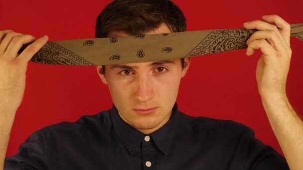 Ein junger Kerl legt ein Kopftuch auf seinen Kopf auf einem isolierten roten Hintergrund — Stockvideo