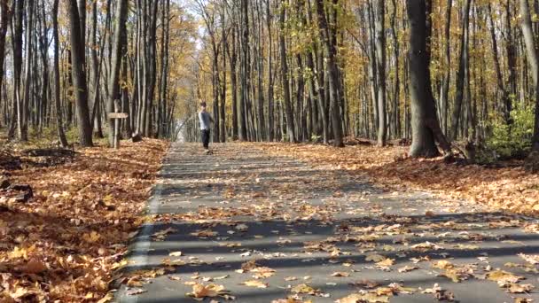 Un hombre desciende sobre un longboard cuesta arriba sobre asfalto cubierto de hojas — Vídeos de Stock