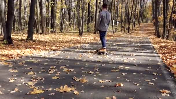 Un homme descend sur un longboard en montée sur de l'asphalte recouvert de feuilles — Video