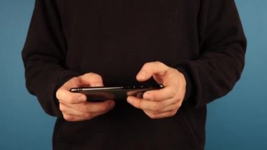 Adam siyah ceketli kameraya bakıyor ve telefonu yatay olarak kullanıyor.