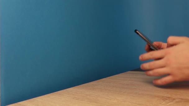 Tangan menggunakan telepon dari samping pada latar belakang biru — Stok Video