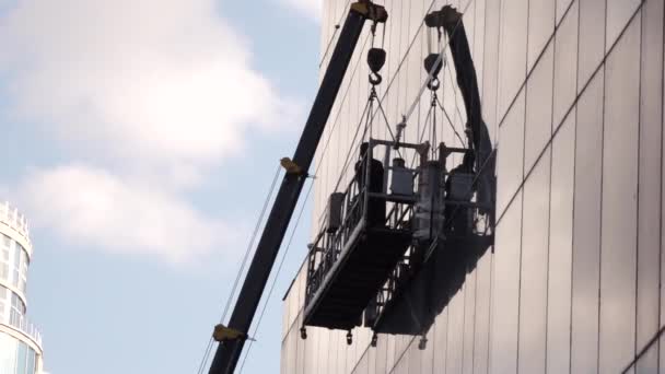 Ein Mann, der auf einer waagerechten Plattform steht und die Fenster reinigt — Stockvideo