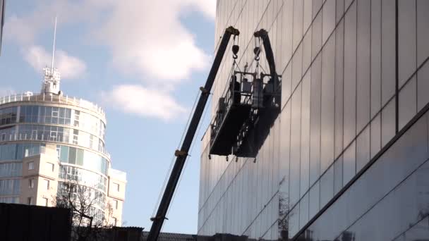 Ein Mann, der auf einer waagerechten Plattform steht und die Fenster reinigt — Stockvideo