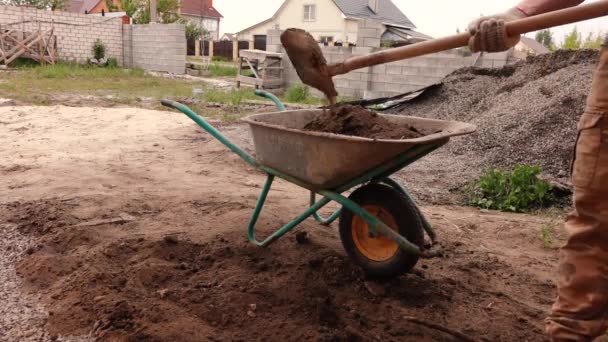 Un hombre llena un carro de construcción con tierra y se lo lleva — Vídeos de Stock