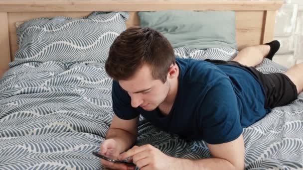 Ένα άτομο είναι ξαπλωμένο στο κρεβάτι και χρησιμοποιεί το τηλέφωνο — Αρχείο Βίντεο