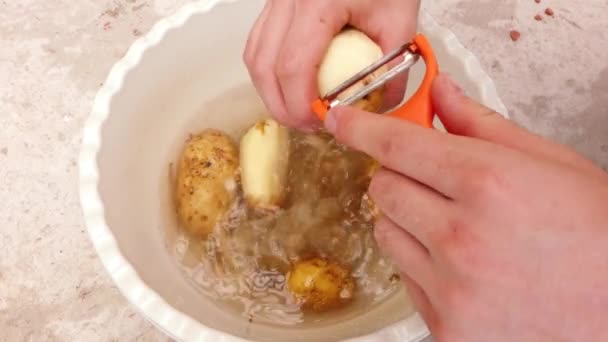 En man skalar potatis och lägger dem i ett handfat — Stockvideo