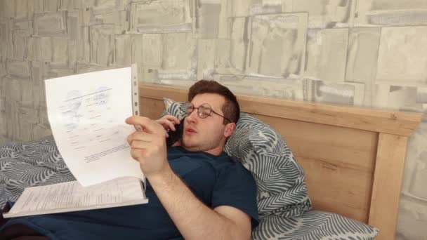 Biznesmen zajmuje się dokumentami leżącymi na łóżku — Wideo stockowe