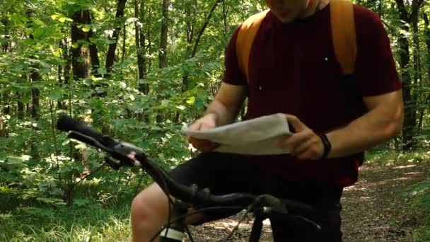 Un hombre en una bicicleta se ha detenido en el bosque y está estudiando un mapa — Vídeos de Stock