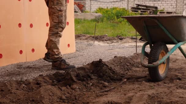 De man met de schop gooit de aarde in een bouwkar — Stockvideo