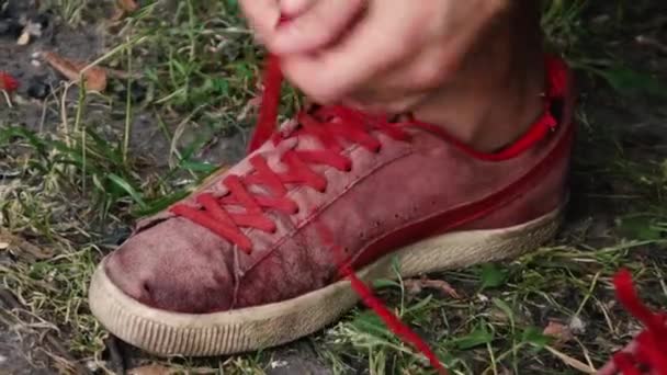 Man bindt de veters van oude rode sneakers terwijl op straat — Stockvideo