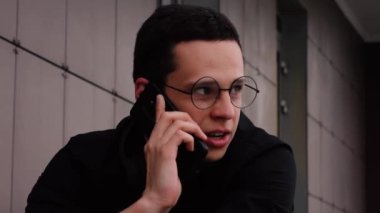 Gözlüklü adam sokakta telefonla konuşuyor.